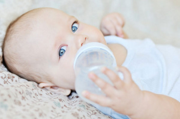 Грудной ребенок пьет воду с бутылочки