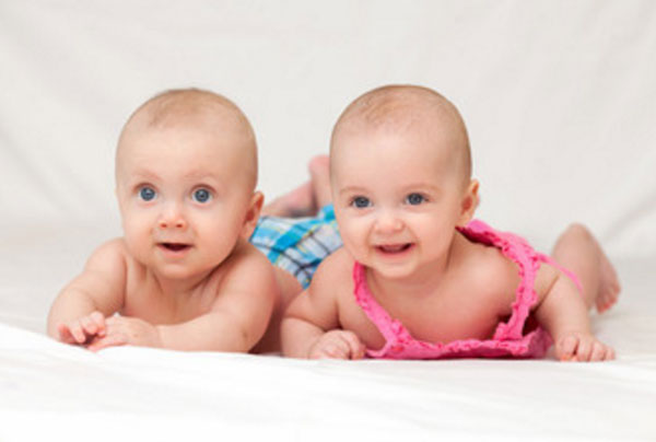 Двойняшки, мальчик и девочка, лежат на животиках